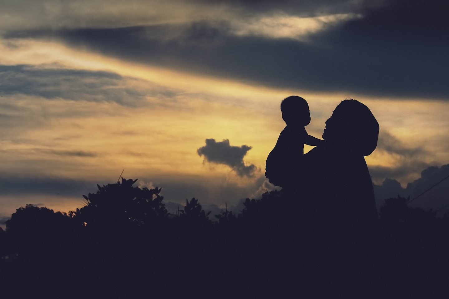 A mother holds her baby against a bright sunset sky.