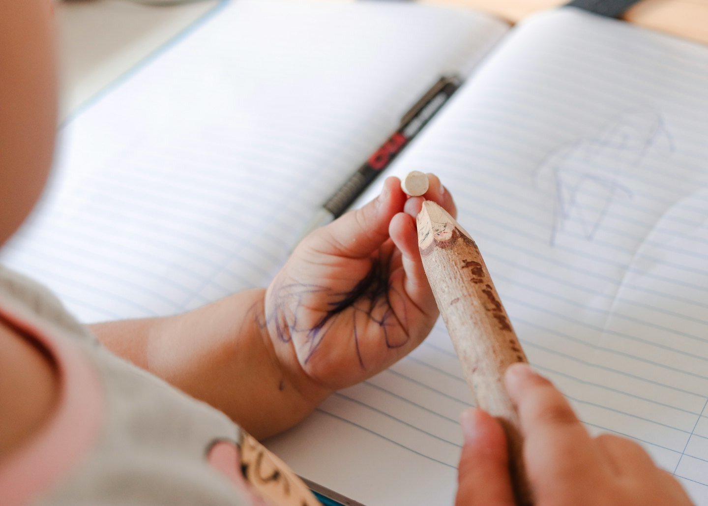 Child holding a pencil and eraser over an open notebook.