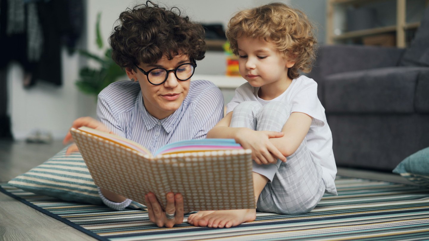 A woman reads a colorful book to a child.